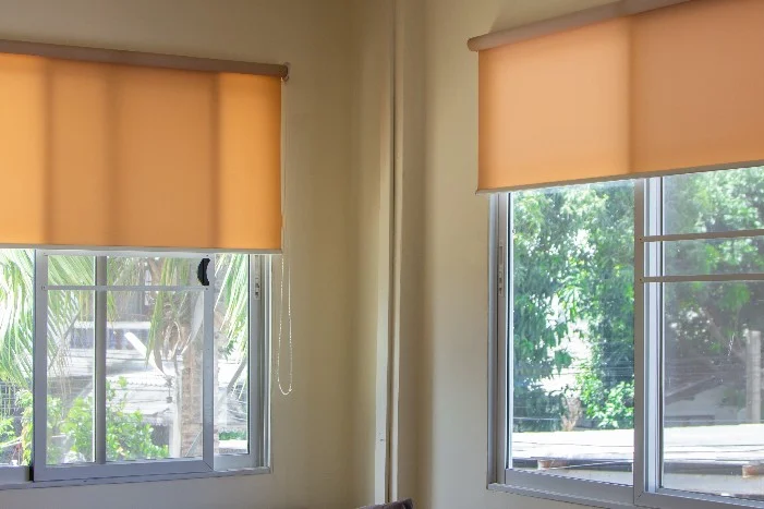 Zwei Fenster mit heruntergelassenen orangefarbenen Rollos.